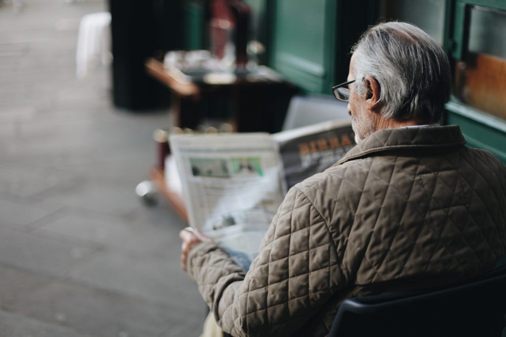 Elderly man with glasses reading newspaper at cafe