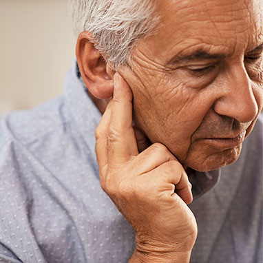 Elderly man holding ear looking upset, hearing loss