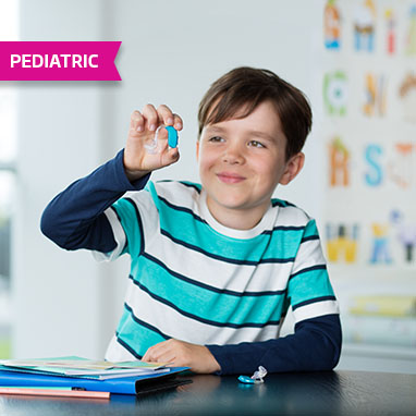 Young male child in classroom holding hearing aid in right hand