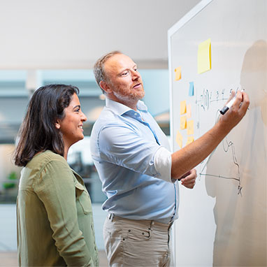 Adult man and woman in front of whiteboard writing and working